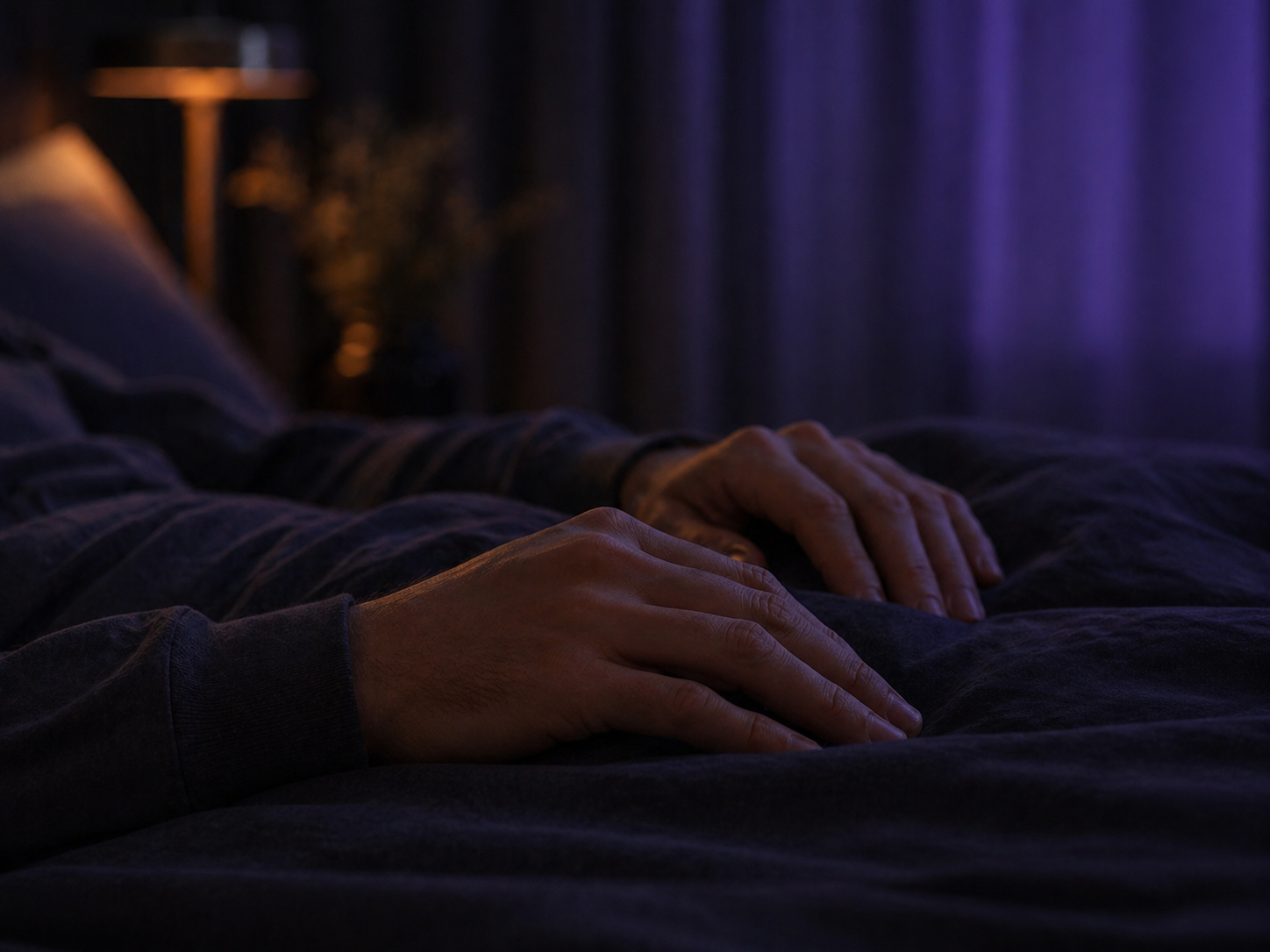 Close de mãos relaxadas sobre um cobertor escuro com luz violeta suave.